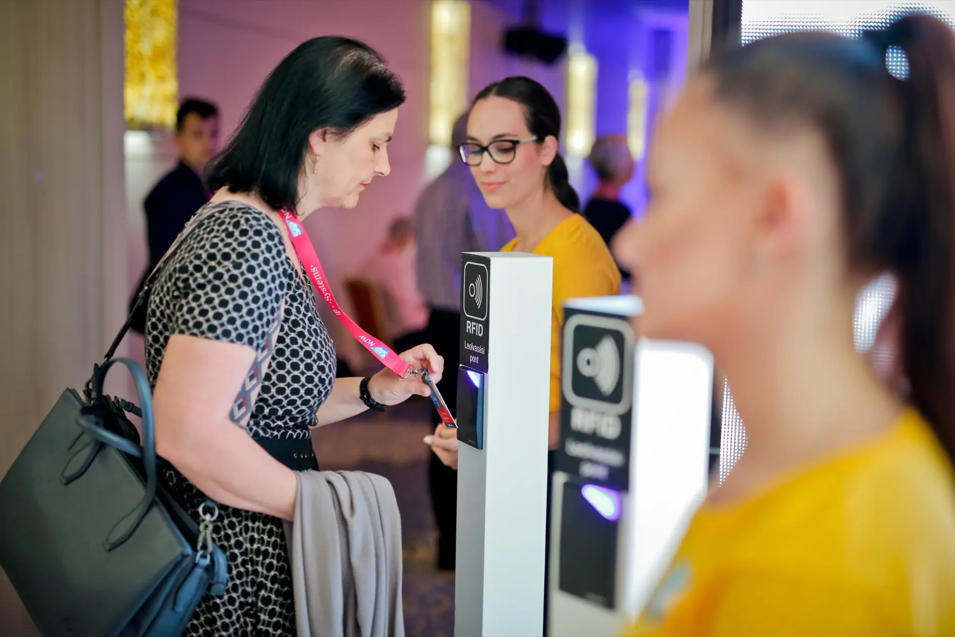 Rendezvényvendég a kártyáját érinti egy RFID leolvasási ponthoz, mellette hostess segít